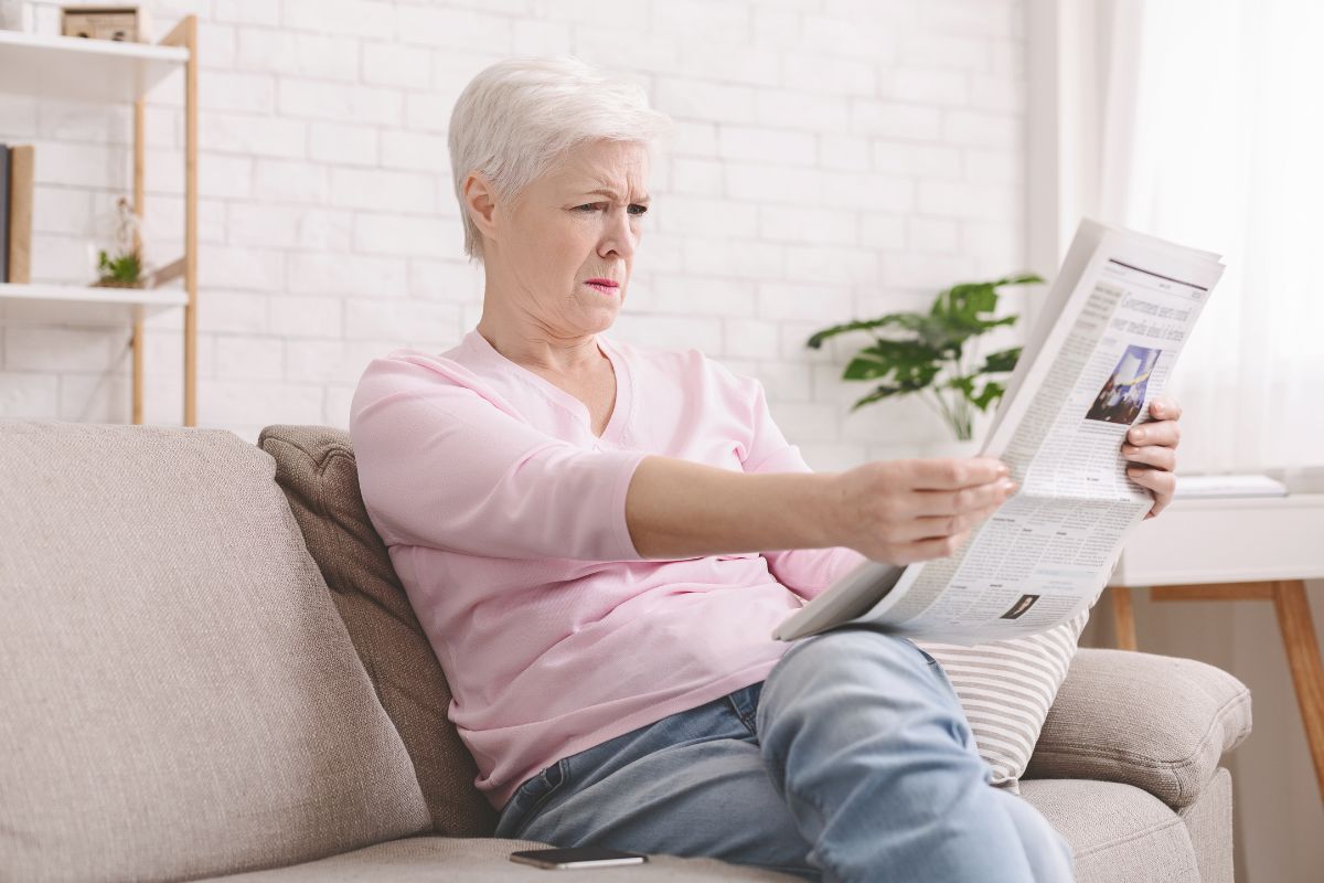 senior-lady-squinting-and-holding-newspaper-far-from-eyes